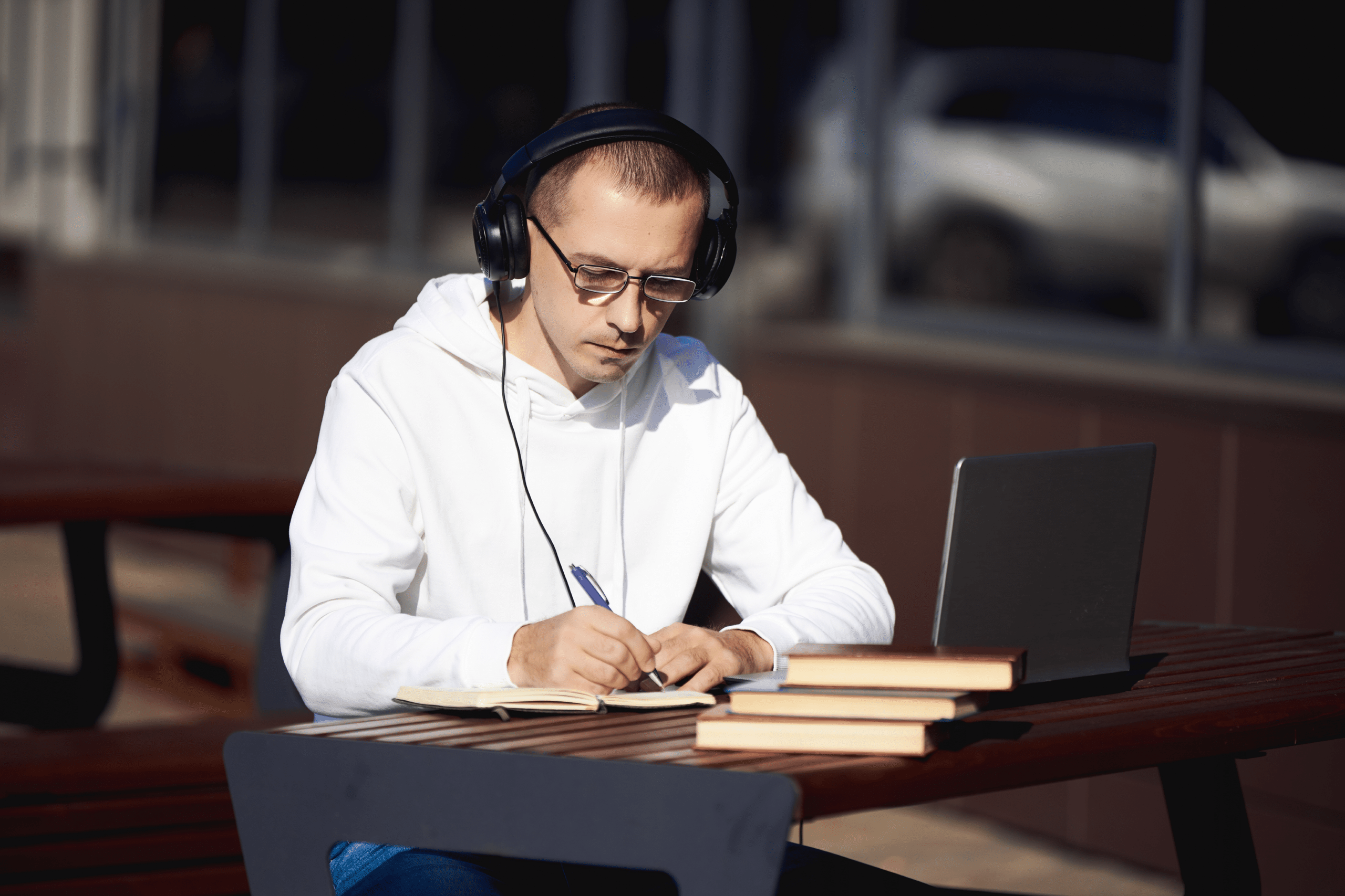 man-with-headphones-is-working-laptop-writing-notebook-sitting-street-table-social-distancing-coronavirus (1)